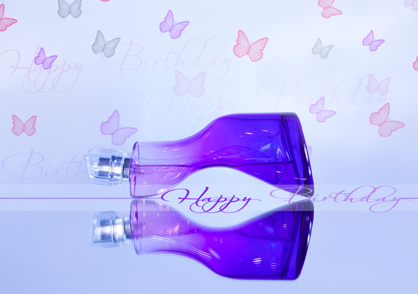 Violette Parfümflasche liegend mit Spiegelbild, im Hintergrund Schmetterlinge, Text "Happy Birthday"