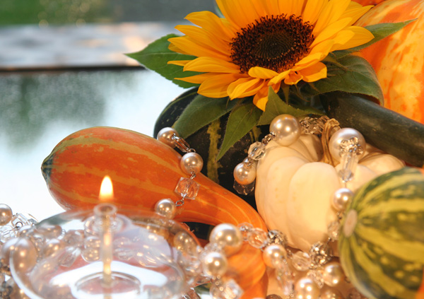 Glaslicht, Kürbis, Sonnenblume und Perlenkette auf Spiegel